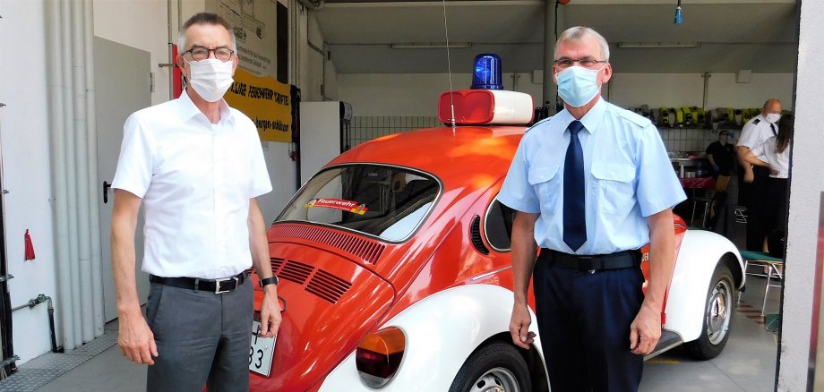 Der Erste Beigeordnete Franz Jirasek mit Werner Hasel vor einem Feuerwehrfahrzeug. Beide tragen Mundschutz.