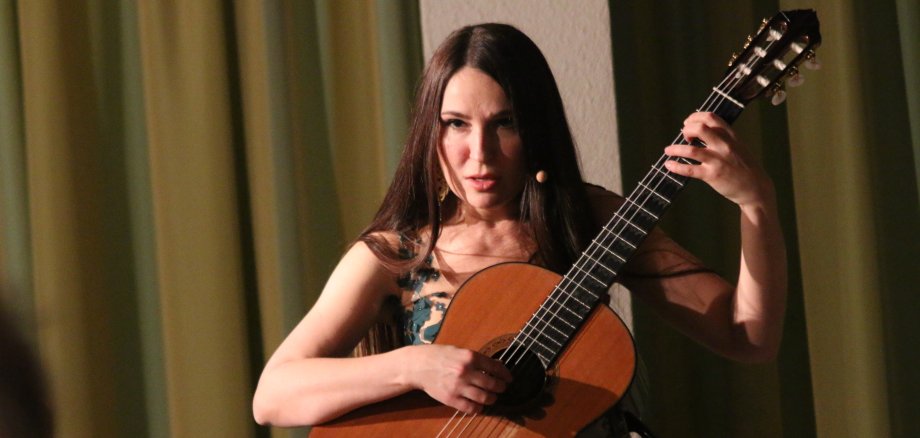 Die Gitarristin Yuliya Lonskaya hält die Gitarre vor sich und spielt mit ernstem Gesichtsausdruck.
