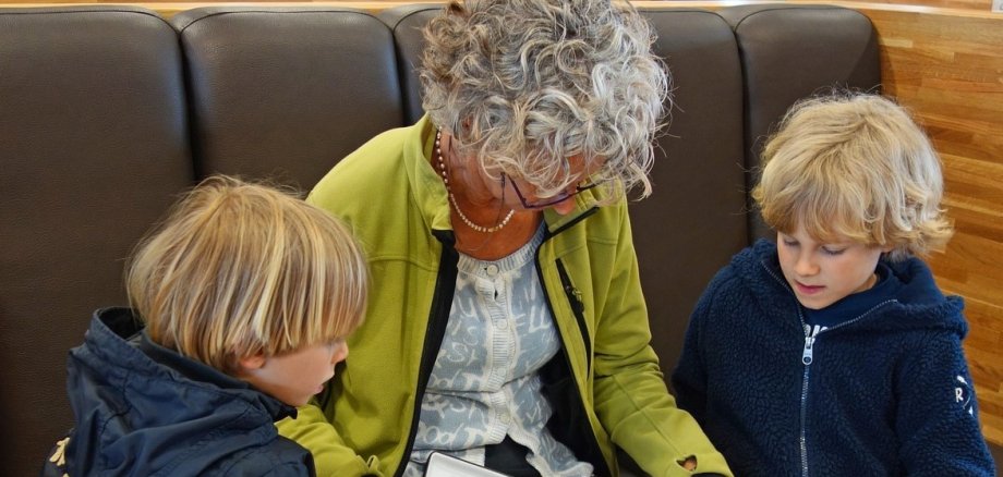 Eine Frau mit grauen Haaren liest zwei Kindern vor.