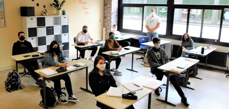 JUgendliche mit Masken sitzen, jeweils alleine an einem Tisch, im Klassenraum.
