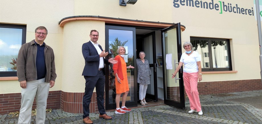 Dr. Fichert, Leiter Kulturforum, Bürgermeister Seitz und drei Damen vom Bücherei-Team vor der Gemeindebücherei am Bahnhof. Sie halten symbolisch die Tür auf.