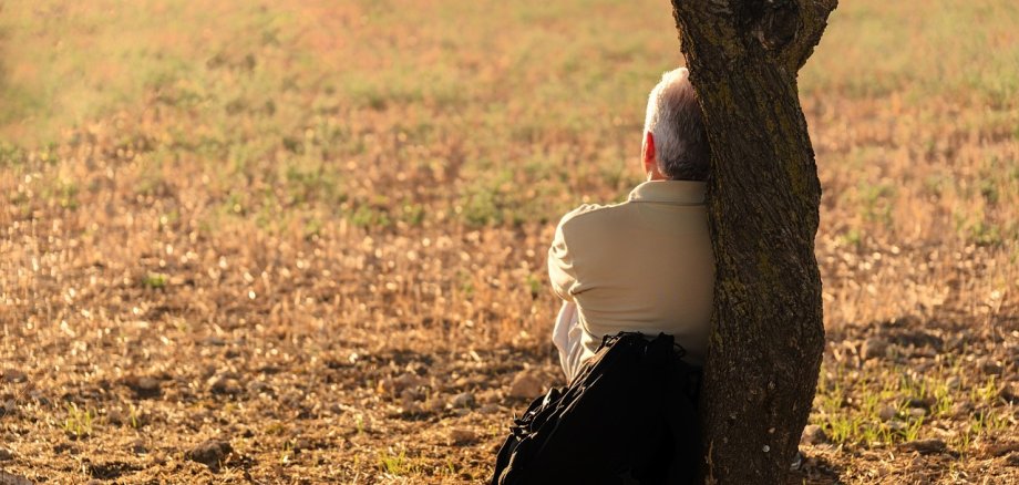 Ein Mann sitzt auf dem Boden an einen Baum gelehnt.