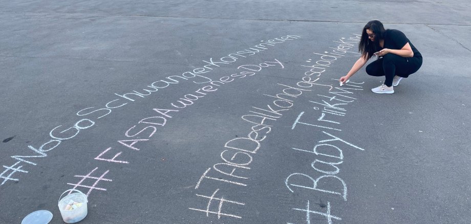 Eine Frau schreibt mit Kreide Schriftzüge gegen Alkohol in der Schwangerschaft auf den Festplatz im Freizeitpark.