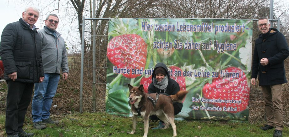 Jirasek, Hoss und Theis vor einem Banner. Eine Spaziergängerin mit Hund kniet davor.