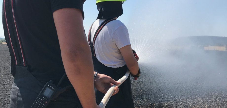 Zwei Wehrleute mit Schlauch löschen einen Feldbrand.