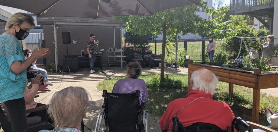 Giovanni LOmbardo singt im Garten, Menschen in Rollstühlen hören zu,