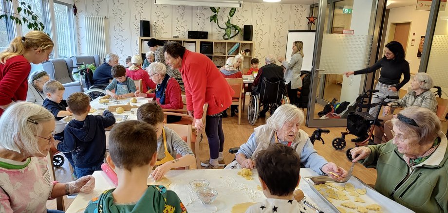 Viel Trubel: Seniorinnen und Kinder rollen an Tischen Teig aus.