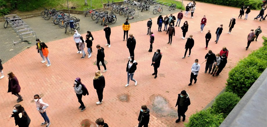 Schüler mit Masken stehen mit Abstand in Schlangen vor der Schule.