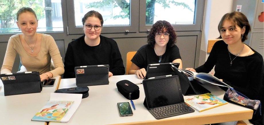 Schülerinnen mit Buch und Tablets.